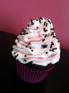 Chocolate cupcake topped with a fresh raspberry buttercream and chocolate sprinkles.