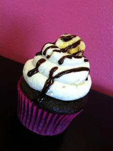 Chocolate cupcake with a banana filling, with a creamy peanut butter buttercream and topped with a drizzle of rich chocolate syrup and a banana chip.